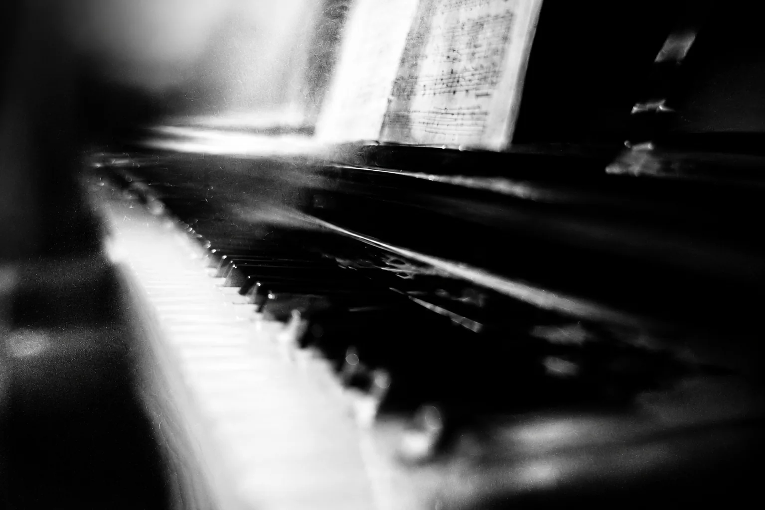 A piano keyboard and open sheet music seen through grain, bloom, and shallow focus.