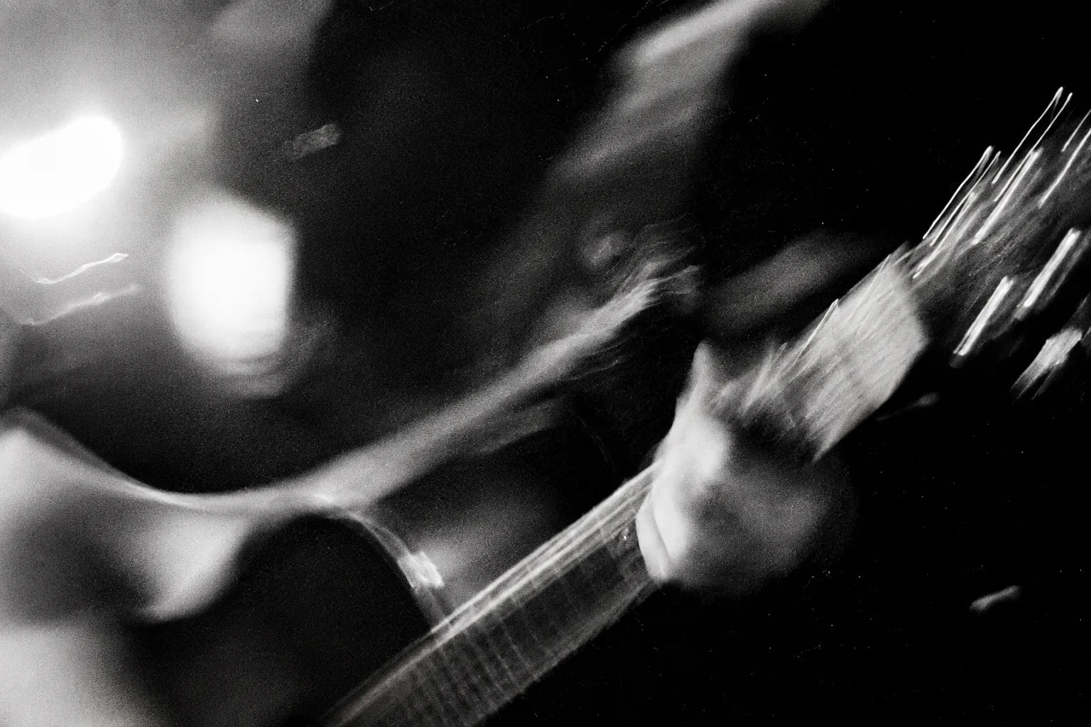 A guitarist's fretting hand and instrument blurred by movement under bright stage lights.